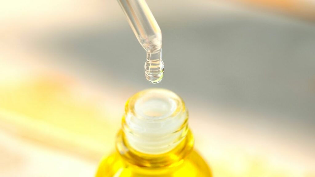 Hellgelbe Flüssigkeit tropft aus einer Pipette in eine gelbe Flasche und illustriert Mineralöl in Kosmetik.